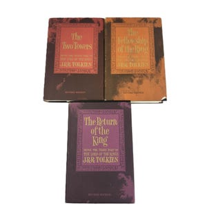 Puede incluir: Tres libros de tapa dura de la trilogía El Señor de los Anillos. Los títulos son "Las Dos Torres", "La Comunidad del Anillo" y "El Retorno del Rey". Cada libro tiene un esquema de color diferente con texto dorado y blanco.