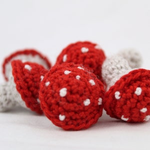 Puede incluir: Cuatro setas de ganchillo con sombreros rojos y puntos blancos y tallos blancos.