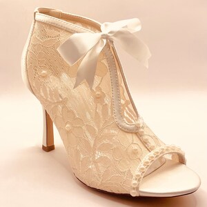 May include: White lace bridal heels with a satin bow and pearl accents.