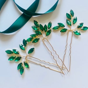 Puede incluir: Tres horquillas doradas con hojas de cristal verde esmeralda. Las horquillas están diseñadas para parecer ramas con hojas.