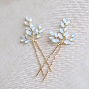 Op de afbeelding: Twee gouden haarspeldjes met witte opaal bladontwerpen. De speldjes zijn delicaat en perfect om elke haarstijl een vleugje glans te geven.