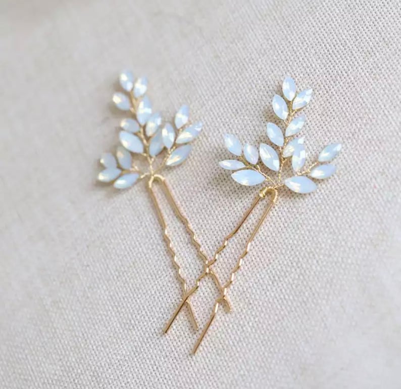 Op de afbeelding: Twee gouden haarspeldjes met witte opaal bladontwerpen. De speldjes zijn delicaat en perfect om elke haarstijl een vleugje glans te geven.
