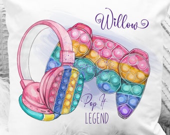 May include: A white pillow with a colorful pop it toy and pink headphones. The pillow has the name "Willow" and the text "Pop It Legend" printed on it.