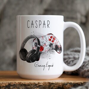 Pu&ograve; includere: Una tazza in ceramica bianca con un'illustrazione in bianco e nero di un controller da gioco e cuffie. La tazza ha il nome "CASPAR" e il testo "Gaming Legend" stampato.