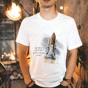 May include: White t-shirt with a watercolor illustration of a space shuttle launching into space. The text "if your flying under the radar you'll never launch into orbit" is printed on the shirt.