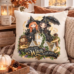 Puede incluir: Un cojín cuadrado con una ilustración gráfica de dos jóvenes brujas con sombreros negros sentadas en el tejado de una casa, acompañadas por dos gatos negros, baúles apilados y el texto There's a little Witch in all of us.