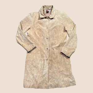 May include: A tan suede coat with a button-up front and a collared neckline. The coat has long sleeves and a knee-length hem. The suede has a textured appearance, and the coat appears to be in good condition.