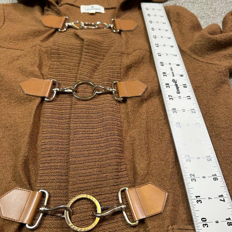 May include: A brown hooded coat with three sets of toggle closures. The closures feature silver metal hardware and brown leather accents. The coat has a ribbed knit section and a soft, textured fabric. A ruler is visible in the image.