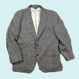 May include: A gray tweed blazer with a two-button closure, notched lapels, and two front pockets. The jacket has elbow patches and a light-colored lining. The blazer is a classic style.