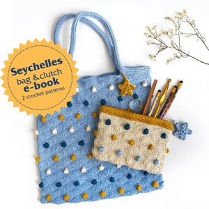 May include: A blue and beige crochet tote bag and matching clutch with yellow, white, and blue pom-poms. The tote bag has a star charm and the clutch has a star charm and a zipper. The text "Seychelles bag & clutch e-book 2 crochet patterns" is on a yellow starburst.