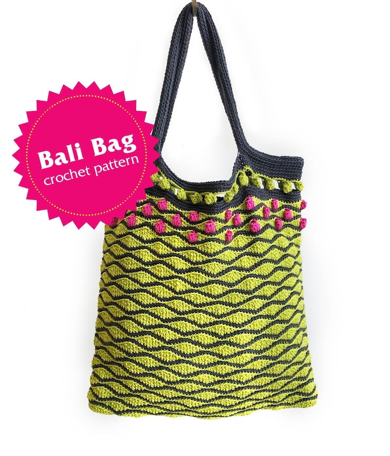 Puede incluir: Una bolsa de mano de crochet verde y negra con pompones rosas alrededor de la parte superior. La bolsa tiene un patr&oacute;n ondulado y el texto "Bali Bag crochet pattern" est&aacute; en una estrella rosa.