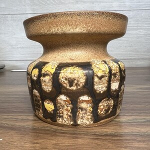 May include: A ceramic vase with a wide, rounded body and a narrow neck. The vase features a brown and tan color scheme with a textured pattern of black, yellow, and white shapes. The vase is likely vintage.