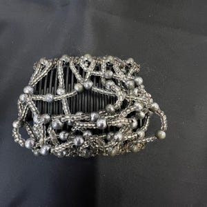 Puede incluir: Una taza de cerámica blanca con un asa negra y el texto "But First, Coffee" en negrita negra. La taza se encuentra sobre un fondo borroso, sugiriendo un ambiente acogedor.