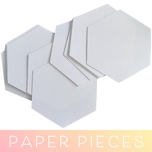 May include: A stack of white hexagon-shaped paper pieces. The paper pieces are arranged in a staggered pattern. The paper pieces are for crafting.