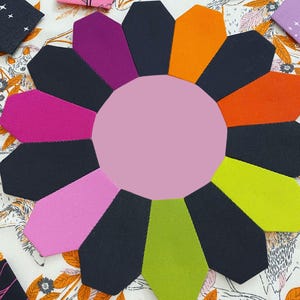 May include: A pink and black fabric flower with 12 petals. The petals are in a variety of colors, including pink, purple, orange, green, and black. The flower is made of fabric scraps and is a great way to use up leftover fabric.