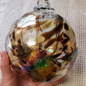 May include: A clear, round glass ornament with brown and gold abstract patterns. The ornament has a loop at the top for hanging. The glass reflects light, creating iridescent colors.