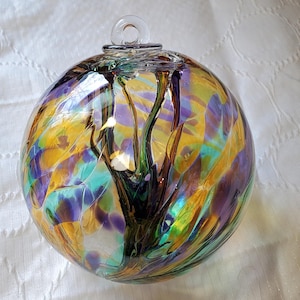 May include: A glass ornament with a swirling pattern of yellow, green, purple, and black. The ornament has a clear glass loop at the top for hanging.
