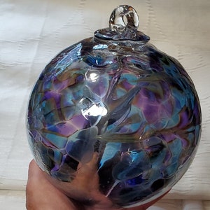 May include: A glass ornament with a swirling pattern of blue, purple, and iridescent colors. The ornament has a clear glass loop at the top for hanging.