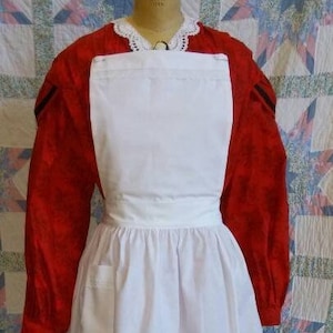 May include: A vintage dress displayed on a mannequin. The dress has a red floral patterned bodice and sleeves, a white apron with a pocket, and a white lace collar. The skirt is red with a white lace trim.