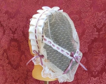 May include: White lace bonnet with a pink ribbon and a white net veil. The bonnet is on a mannequin head.
