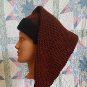 May include: A brown crocheted hat with a black brim and a black tassel. The hat is worn on a mannequin's head.