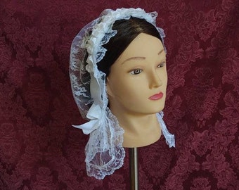 Puede incluir: Un gorro de encaje blanco con una cinta de satén. El gorro se lleva en una cabeza de maniquí sobre un fondo burdeos.