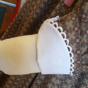 May include: A brown and white checkered dress with a white lace trim on the sleeve. The dress has a pink ribbon detail.