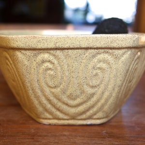 May include: A yellow ceramic mixing bowl with a speckled glaze and a heart-shaped design. The bowl is empty.