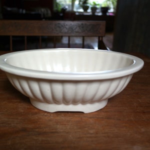 May include: A white ceramic bowl with a fluted design. The bowl is sitting on a wooden table.