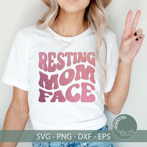 Puede incluir: Una camiseta blanca con un diseño de purpurina rosa y blanca que dice "Resting Mom Face" en una fuente retro.
