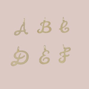 May include: A collection of six gold-toned metal letter charms featuring the uppercase letters A, B, C, D, E, and F. Each charm is designed in a cursive script font with a textured surface and includes a small jump ring at the top for attachment.