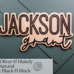 May include: A custom wooden wall sign featuring the name JACKSON in a bold, sans-serif font and the name grant in a cursive script. The letters are black and mounted onto a natural light-coloured wood backing with a cutout shape.