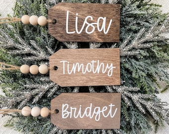 May include: Three wooden ornaments with names "Lisa", "Timothy", and "Bridget" written in white paint. Each ornament has a string with wooden beads attached.