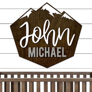 May include: A wooden sign with a mountain range design and the name "John Michael" in white and gray lettering.