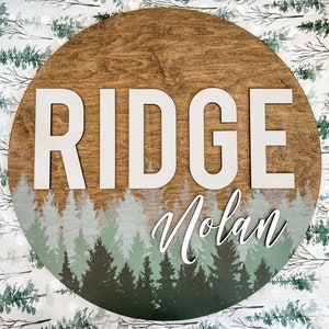 May include: A round wooden sign with a forest scene and the name "Ridge Nolan" written in white letters.