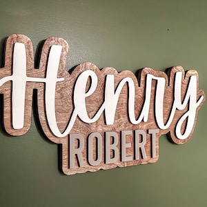 May include: A wooden sign with the names "Henry Robert" in white and gray lettering. The sign has a rustic wood grain texture.