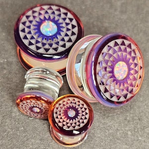May include: Set of four glass ear gauges with a mandala design and iridescent opal accents. The gauges are in shades of purple, pink, and orange.