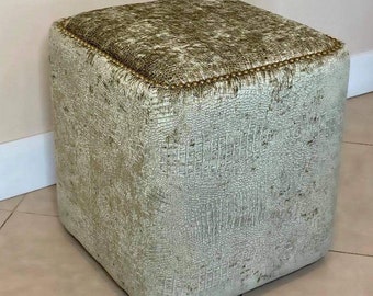 May include: A square ottoman with a light green, textured fabric upholstery. The ottoman has a gold trim around the top edge.