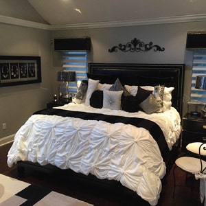 May include: A black and white bedroom with a large bed with a white comforter and black pillows. There are two black lamps on nightstands next to the bed. The walls are painted a light gray color.