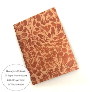 May include: A rectangular notebook with a rust-orange and tan floral pattern cover. A circular white graphic overlay contains the text: Choose from 12 Sizes & 34 Paper Pattern Options 28lb/104gsm Paper in White or Cream.