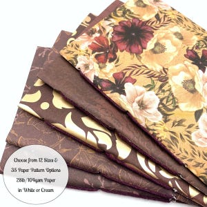 May include: A stack of journals with floral and patterned covers. The top journal features a cream background with red and cream flowers. The other journals have brown and gold designs. The text on the image reads: "Choose from 12 Sizes & 35 Paper Pattern Options 28lb/104gsm Paper in White or Cream."