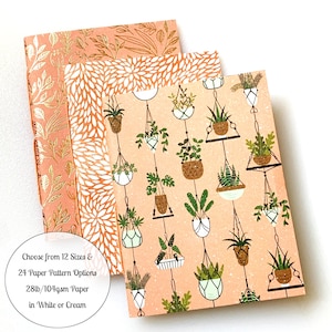 May include: Three notebooks with different patterns. The front cover of each notebook features a pink background with a repeating pattern of hanging plants. The text on the bottom of the image reads: "Choose from 12 Sizes & 24 Paper Pattern Options 28lb/104gsm Paper in White or Cream".