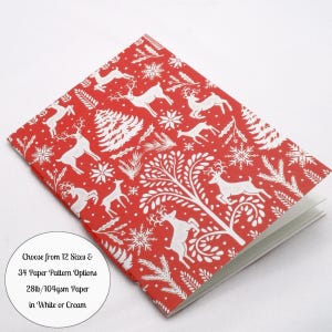 May include: A red notebook with a white repeating pattern of reindeer, pine trees, and snowflakes. A circular white label on the cover reads: Choose from 12 Sizes & 34 Paper Pattern Options 28lb/104gsm Paper in White or Cream.
