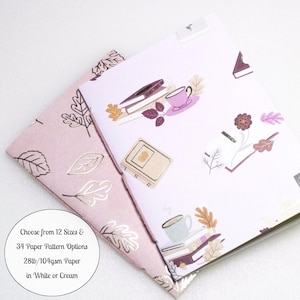 May include: Two notebooks with soft covers. One cover is light pink with metallic foil leaf outlines. The other is white with a pattern of books, cups, and leaves. Text on the image reads: Choose from 12 Sizes & 34 Paper Pattern Options 28lb/104gsm Paper in White or Cream.