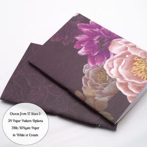 May include: Two notebooks with dark purple covers featuring large pink and purple floral illustrations. A circular white label displays the text: Choose from 12 Sizes & 34 Paper Pattern Options 28lb/104gsm Paper in White or Cream.