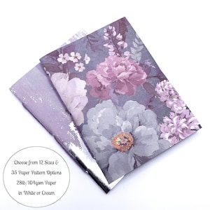 May include: Two floral patterned papers with a purple and white color scheme. The top paper has a large flower design in shades of purple and white. The bottom paper is a solid light purple with a silver edge. Text on the image reads: Choose from 12 Sizes & 35 Paper Pattern Options 28lb/104gsm Paper in White or Cream.