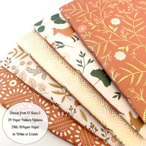 May include: A stack of six patterned paper sheets in various shades of orange, cream, and gold. The paper features floral and geometric designs. The text on the paper reads: "Choose from 12 Sizes & 24 Paper Pattern Options 28lb/104gsm Paper in White or Cream".