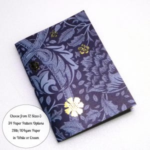 May include: A rectangular notebook with a dark blue and light blue floral pattern cover, featuring gold foil flower accents. A circular white text overlay states: Choose from 12 Sizes & 34 Paper Pattern Options, 28lb/104gsm Paper in White or Cream.