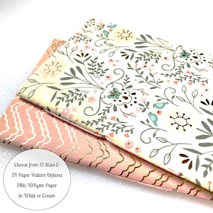 May include: Two sheets of paper with a floral pattern. The top sheet has a white background with pink and gray flowers, green leaves, and blue birds. The bottom sheet has a pink background with a wavy gold pattern. The text on the image reads: "Choose from 12 Sizes & 24 Paper Pattern Options 28lb/104gsm Paper in White or Cream".