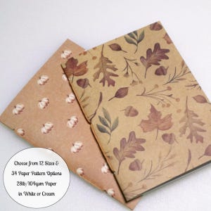 May include: Two notebooks with kraft paper covers. One features a pattern of small white pumpkins, the other a pattern of brown autumn leaves and acorns. Text on the image reads: Choose from 12 Sizes & 34 Paper Pattern Options 28lb/104gsm Paper in White or Cream.